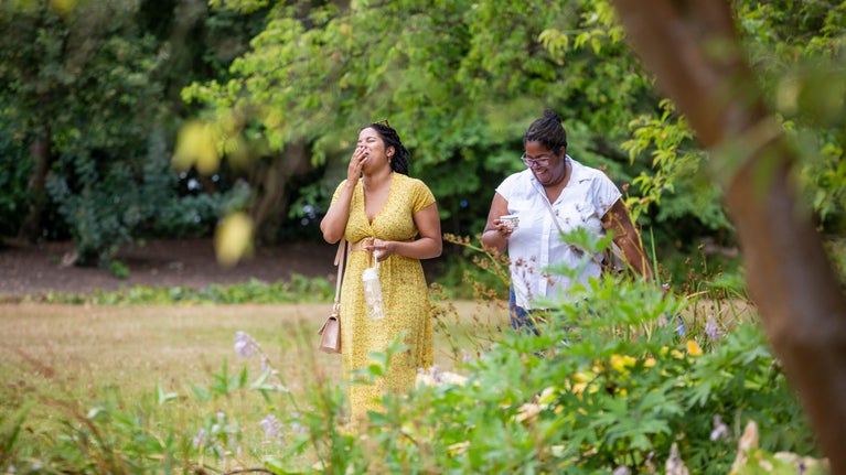 Two visitors walking in the garden, both laughing whilst holding an ice cream at Cliveden in Buckinghamshire